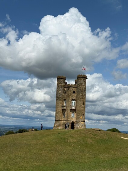 A historic stone castle with two towers, a flag, and a grassy hill under a cloudy sky. 5