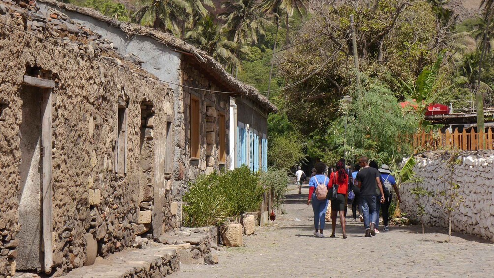 A rustic village with stone buildings, a paved path, and people walking. 5