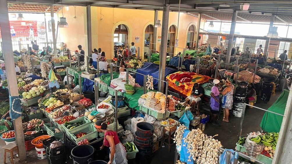 A bustling indoor market with various stalls selling fruits, vegetables, and other goods. 1