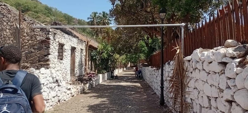 A narrow stone pathway flanked by rustic buildings, a wooden fence, and a clear sky. 2