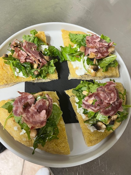 A plate of bruschetta topped with arugula, prosciutto, and mushrooms. 1