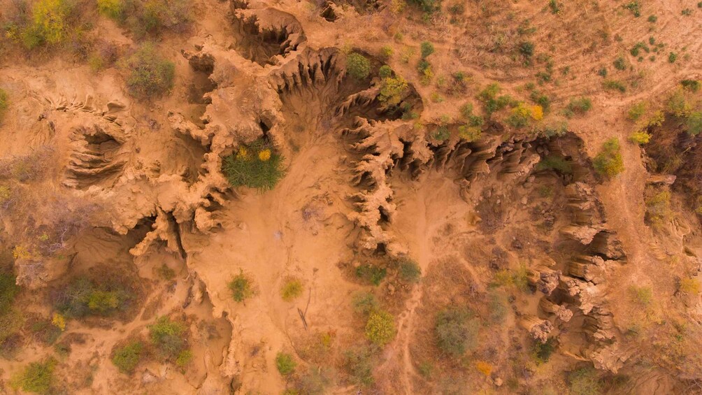 A rugged terrain with a large, circular depression surrounded by eroded rock formations and sparse vegetation. 3