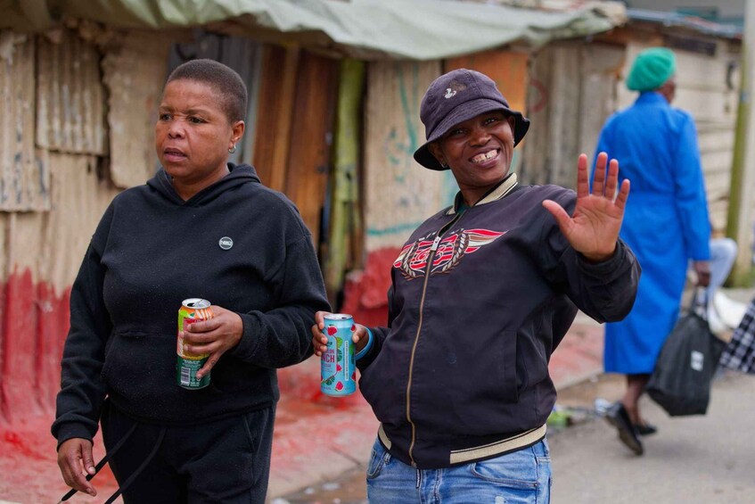 Two people walking on a street, one holding a can and the other waving. 4