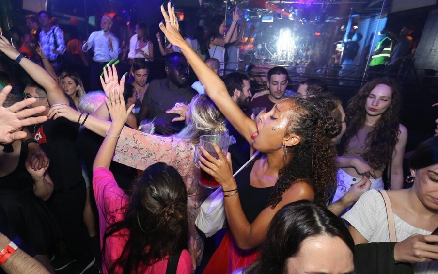 A crowded indoor event with people holding drinks and raising their hands. 4