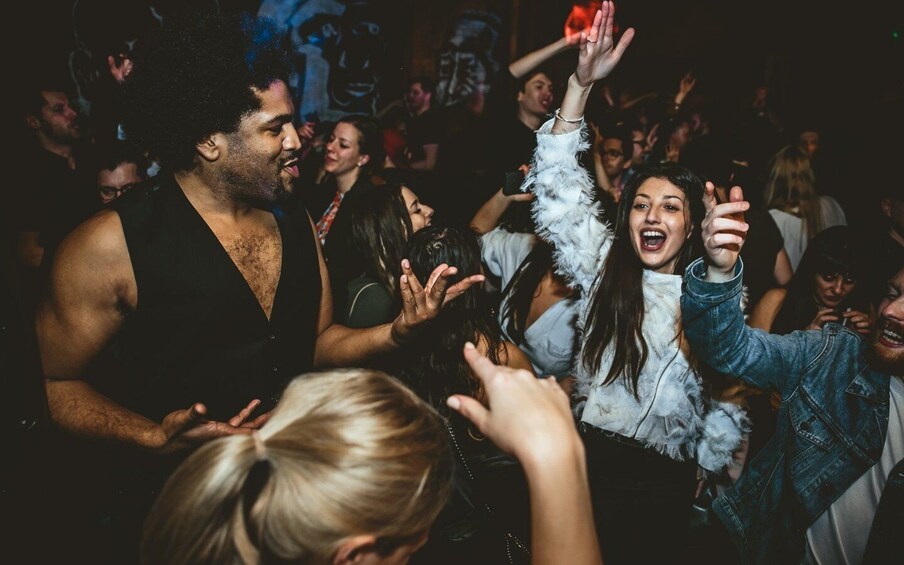 A crowded indoor event with people dancing and raising their hands. 2