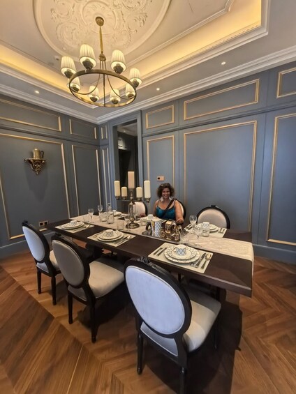 A dining room with a large table set for a meal, elegant chairs, a chandelier, and decorative wall paneling. 2