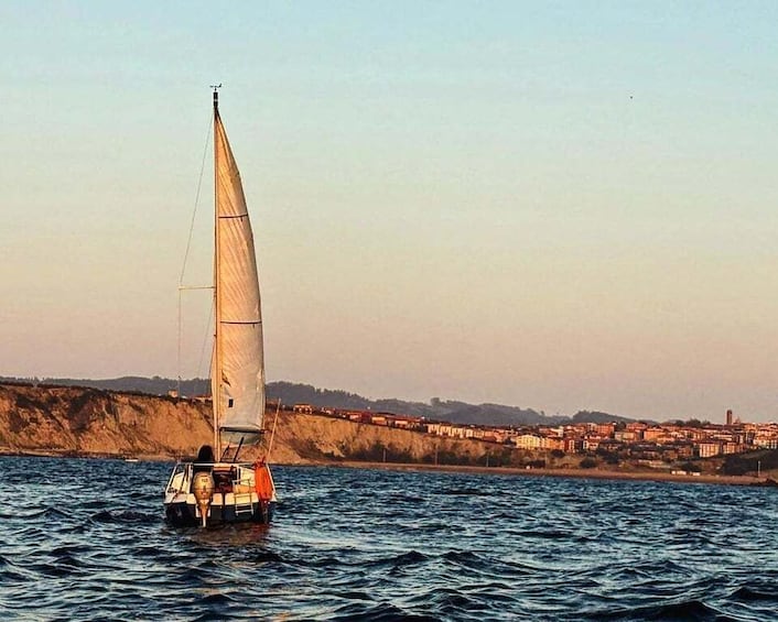 A sailboat on calm waters with a coastal town in the background. 1