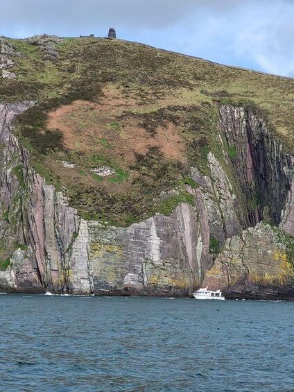 A coastal landscape with a rocky cliff, a grassy hill, and a boat in the water. 2