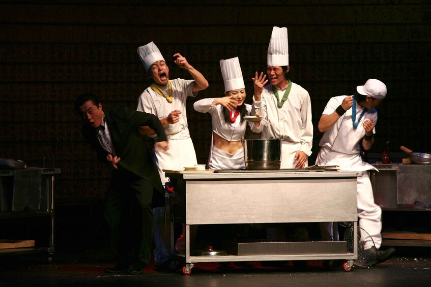 A group of chefs in white uniforms and hats, some with medals, on a stage with a pot and a pan. 4