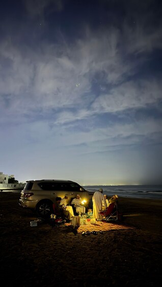 A group of people gathered on a beach at night with a car nearby. 1