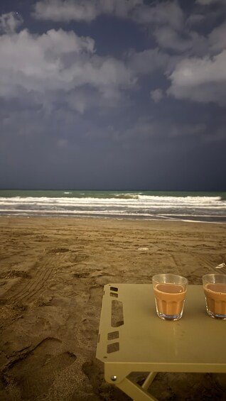 A beach with two glasses of a beverage on a table, and the ocean in the background. 2