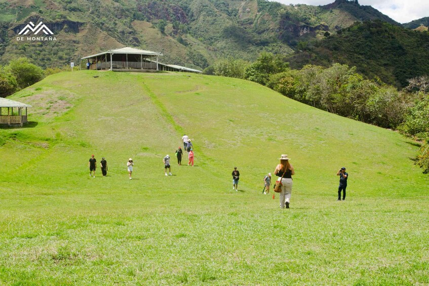 A grassy hill with a covered structure at the top and people walking around. 4