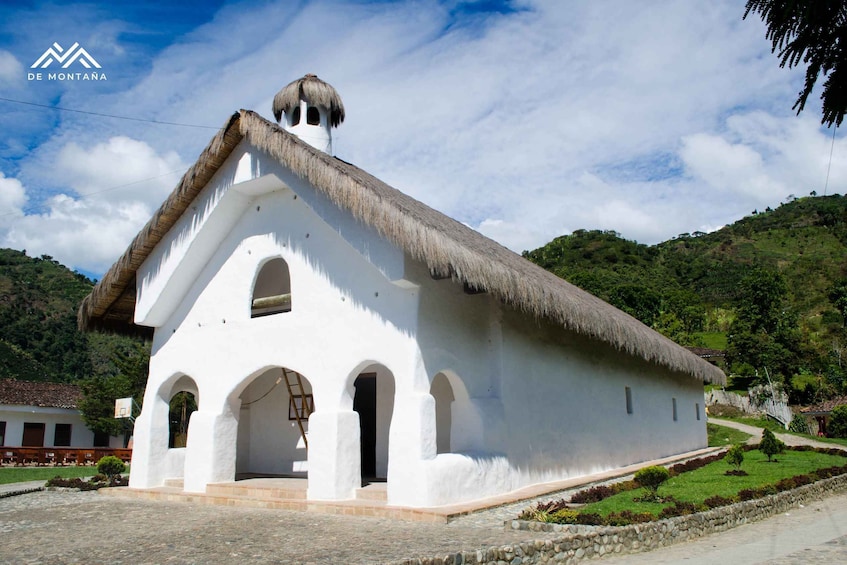 A white building with a thatched roof, set against a backdrop of lush greenery and hills. 3