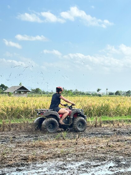 A person riding an ATV in a field with a house in the background. 2