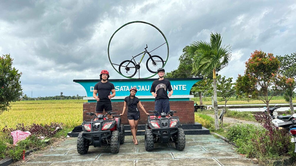 Three people standing in front of a sign with a bicycle and ATVs. 1