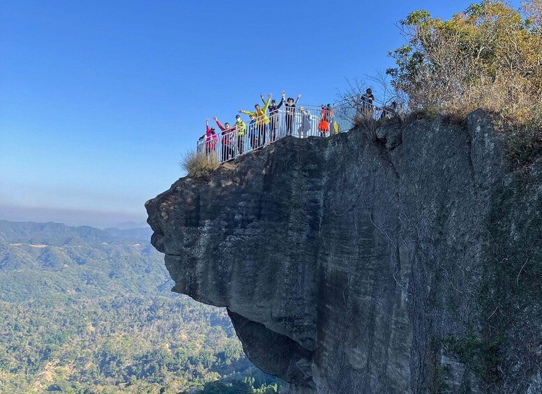 A group of people standing on a cliff edge with a forested valley below. 2