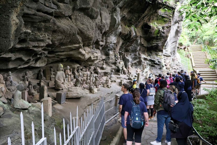 A group of people standing on a stone path beside a rocky cliff with numerous statues. 1