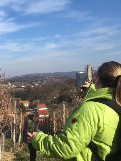 A person in a green jacket taking a photo of a landscape with houses and vineyards. 4