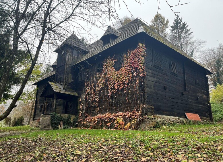 A rustic wooden house with a steep roof, surrounded by trees and covered with autumn leaves. 5