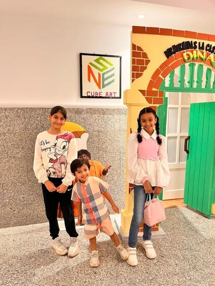 A group of people in a room with a sign that reads 'NE CUBE ART' and a colorful door with the text 'BIENVENIDOS LA CASA DINA'. 2