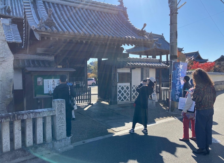 A traditional Japanese gate with a tiled roof, a stone base, and a wooden fence. 2