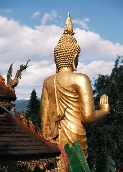 A golden Buddha statue with intricate carvings, set against a backdrop of a clear sky and lush greenery. 3