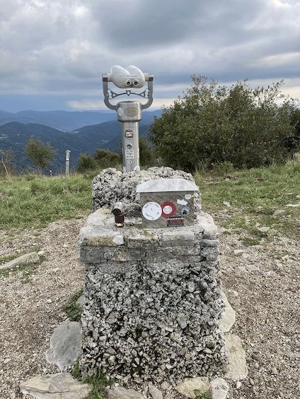 A mountain peak with a metal structure on top, surrounded by rocky terrain and greenery. 2