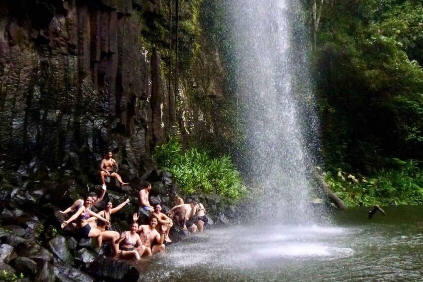 A group of people sitting on rocks by a waterfall in a forested area. 5