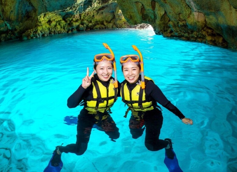 Two people scuba diving in a clear blue pool with rocky walls. 2