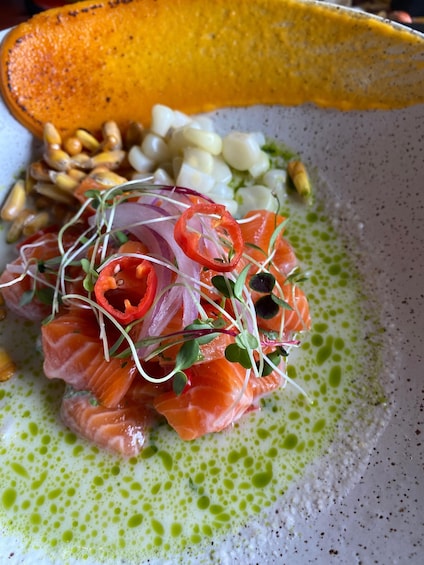 A dish with salmon, red onion, and microgreens on a plate with a green sauce. 1