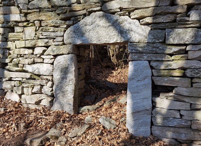 A stone structure with a rounded archway, surrounded by dry leaves and a stone wall. 5