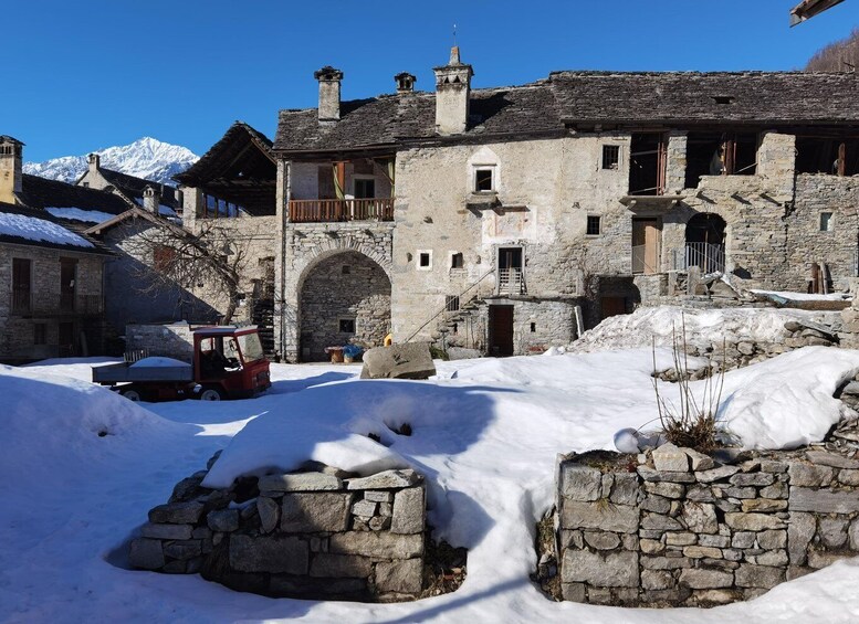 A snow-covered village with stone buildings and a red vehicle parked in the foreground. 4