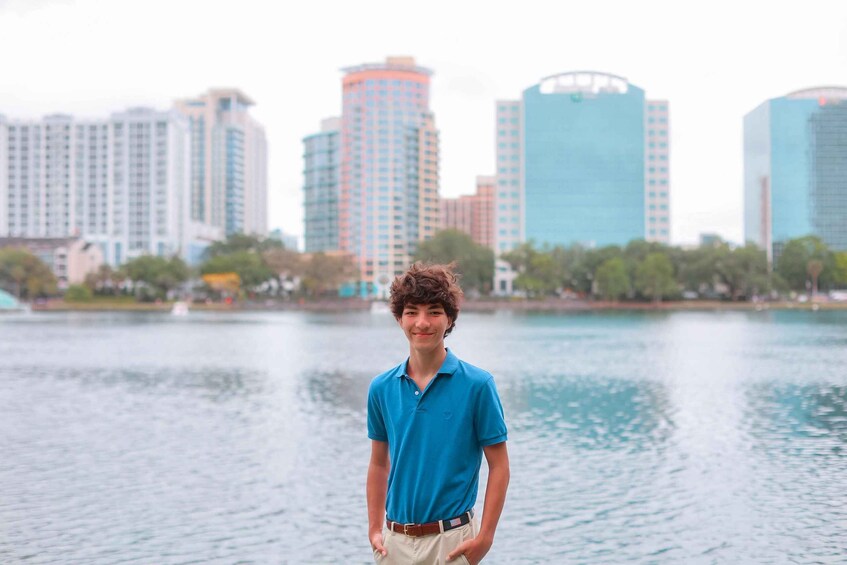 A young man in a blue shirt standing by a body of water with a city skyline in the background. 2