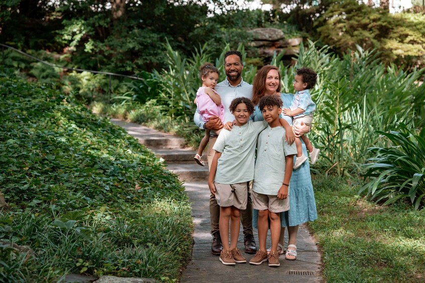 A family of six on a garden path surrounded by lush greenery. 1
