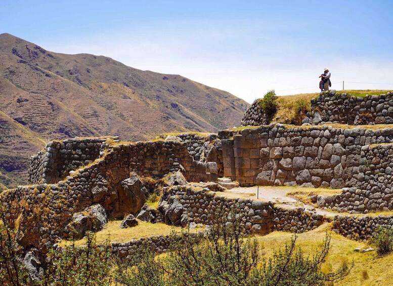Ancient stone ruins with a person standing on a hill overlooking the site. 2