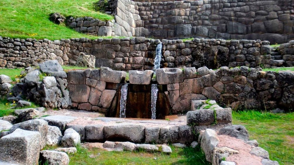 A stone structure with a central water feature, surrounded by grass and additional stone walls. 4