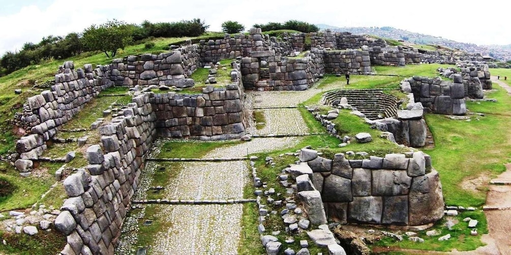 Ancient stone ruins with a circular layout, surrounded by grassy areas and distant hills. 1