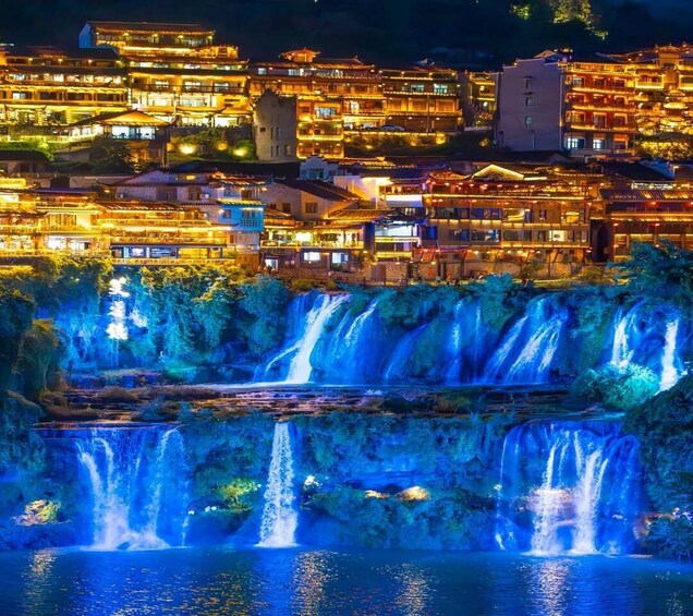A nighttime view of a town with illuminated buildings and a series of cascading waterfalls. 5