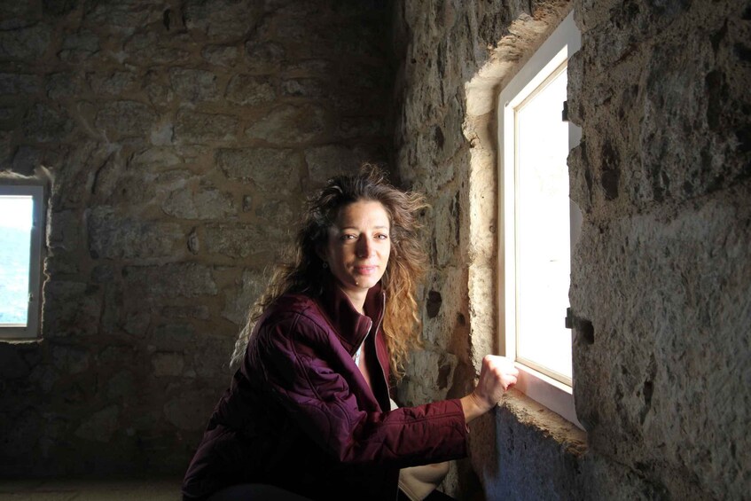 A person crouching near a stone wall with a window. 3