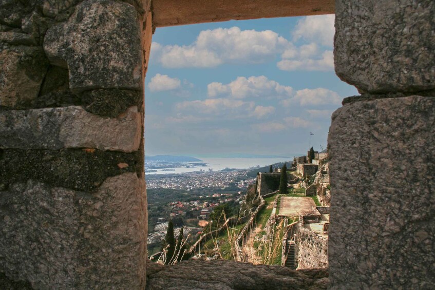 A stone archway framing a view of a coastal city with ancient ruins and a distant shoreline. 4