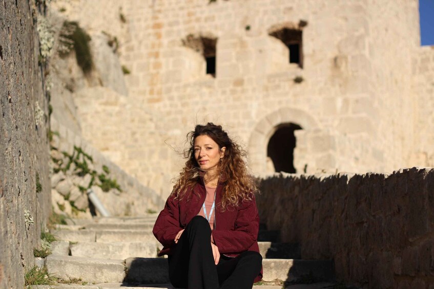 A person sitting on stone steps in front of a historic stone building with arched windows. 1