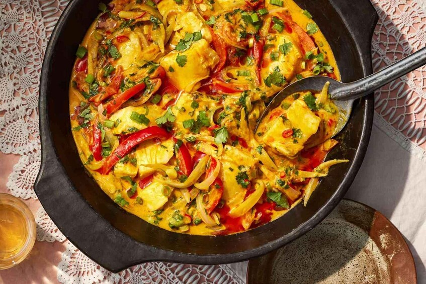 Une poêle contenant un plat de curry à base de poulet, de poivrons et d’oignons, garni d’herbes aromatiques. 2