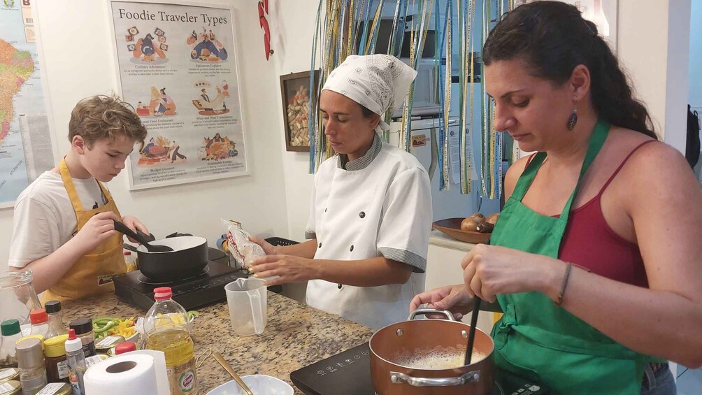Trois personnes préparent un repas dans une cuisine, avec divers ingrédients et ustensiles disposés sur le plan de travail. 4