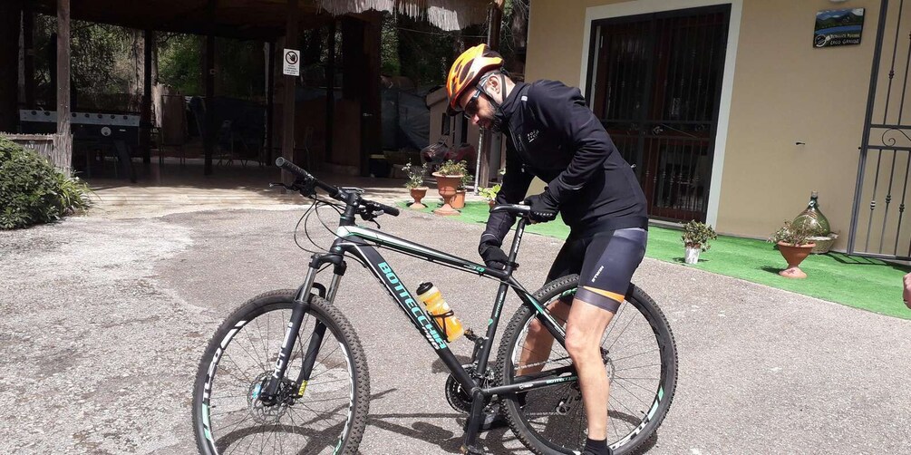 A person adjusting a mountain bike in front of a building with a sign. 1
