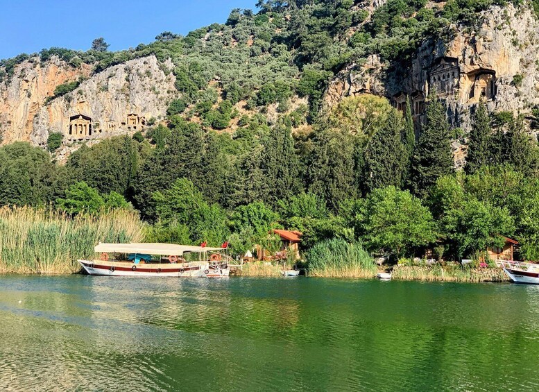 A lake with boats, a cliff with ancient ruins, and lush greenery. 2