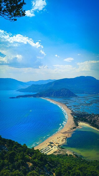 A coastal landscape with a clear blue sea, a sandy beach, and a mountainous backdrop. 5