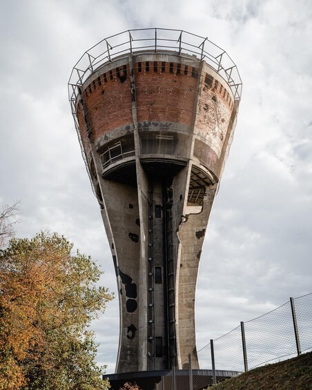A tall, cylindrical structure with a brick exterior and metal framework, surrounded by a chain-link fence. 1