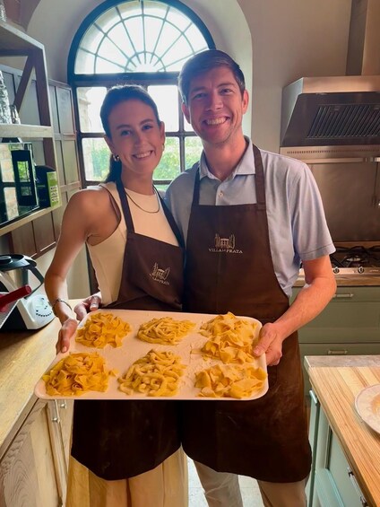 Two people in a kitchen holding a tray of pasta. 4