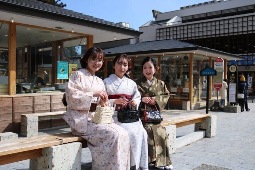 Three people sitting on a bench in front of a building with a sign that reads '84'. 1