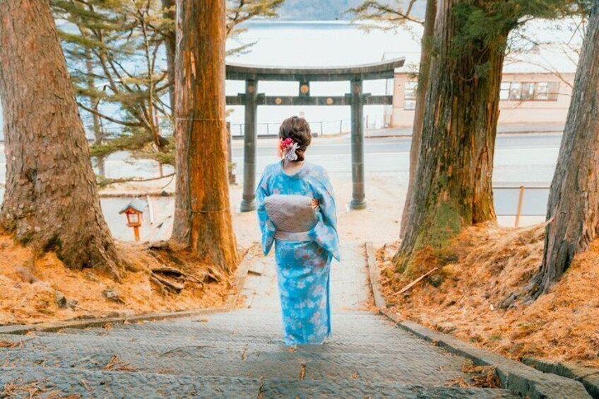 A person in a blue kimono walking on a stone path surrounded by trees. 3